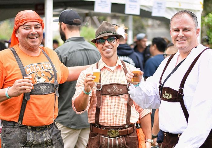 Three men gathered around dressed in lederhosen holding steins during Craftoberfest an Oktoberfest event in Pasadena CA